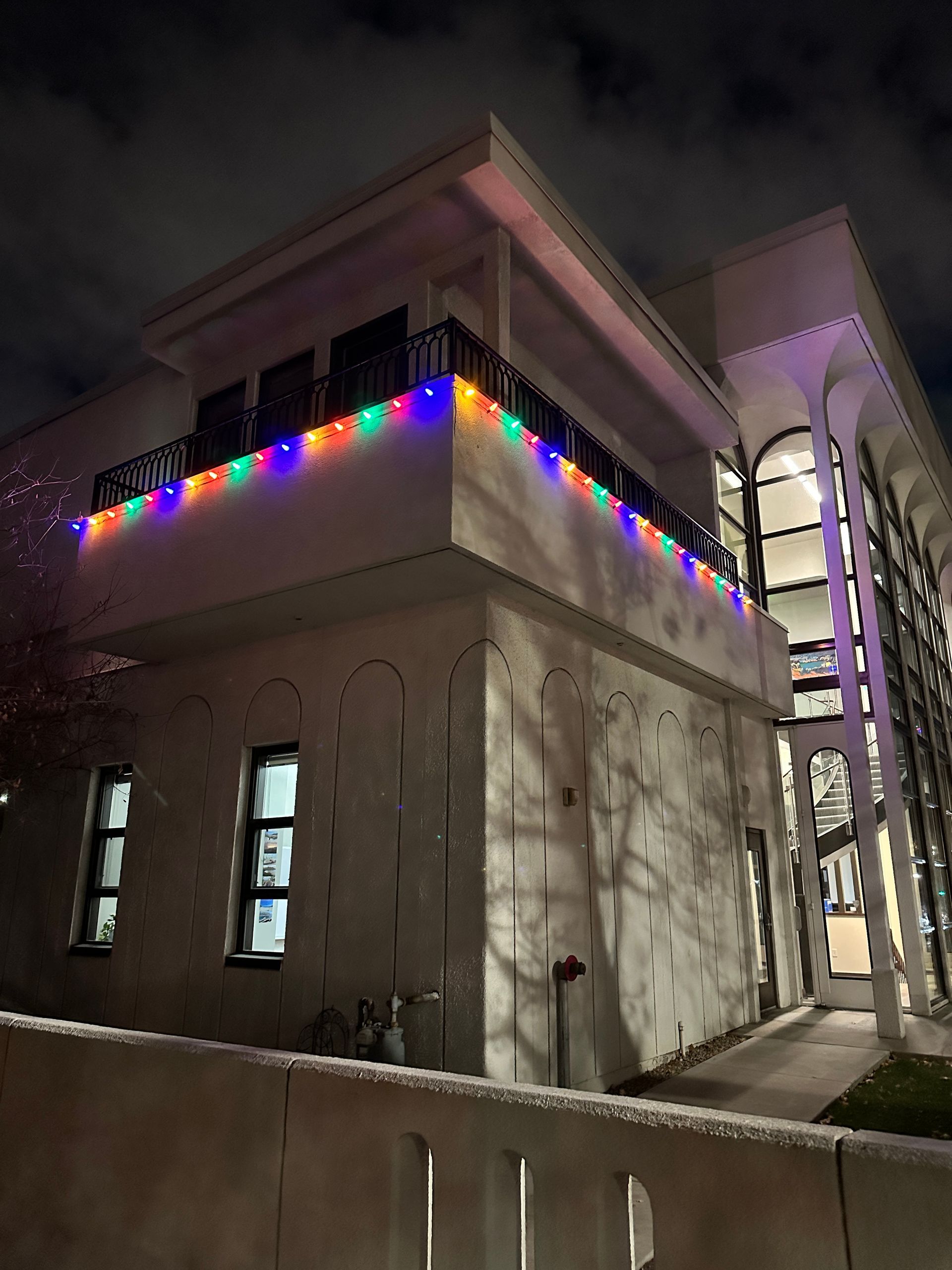 A white building with balcony decorated with colorful lights at night.