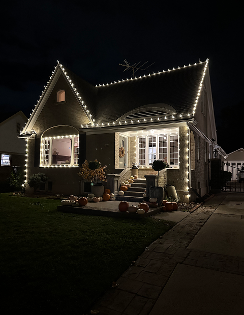 A house is decorated with christmas lights and pumpkins at night.