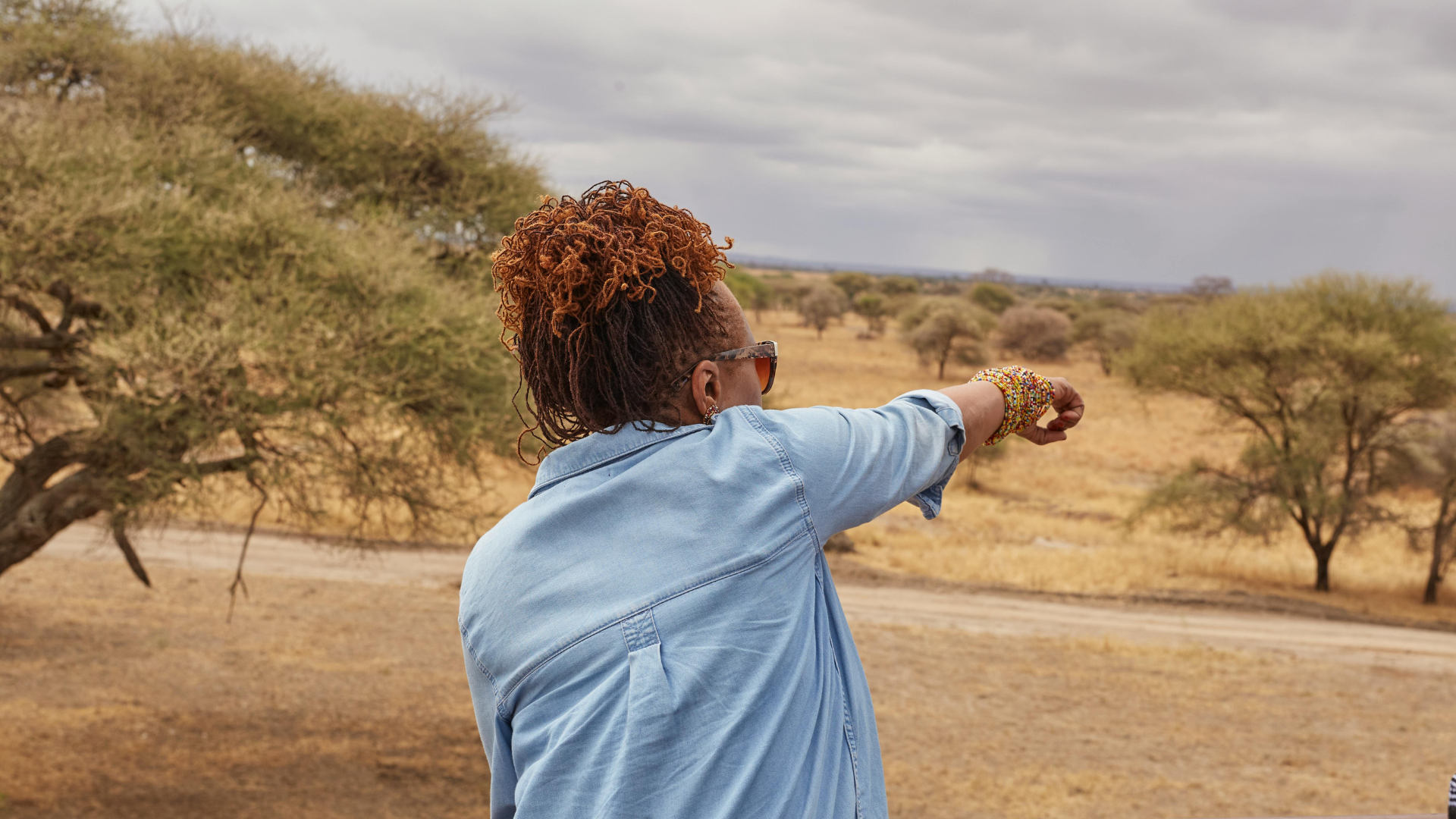 Woman in denim points toward savanna.