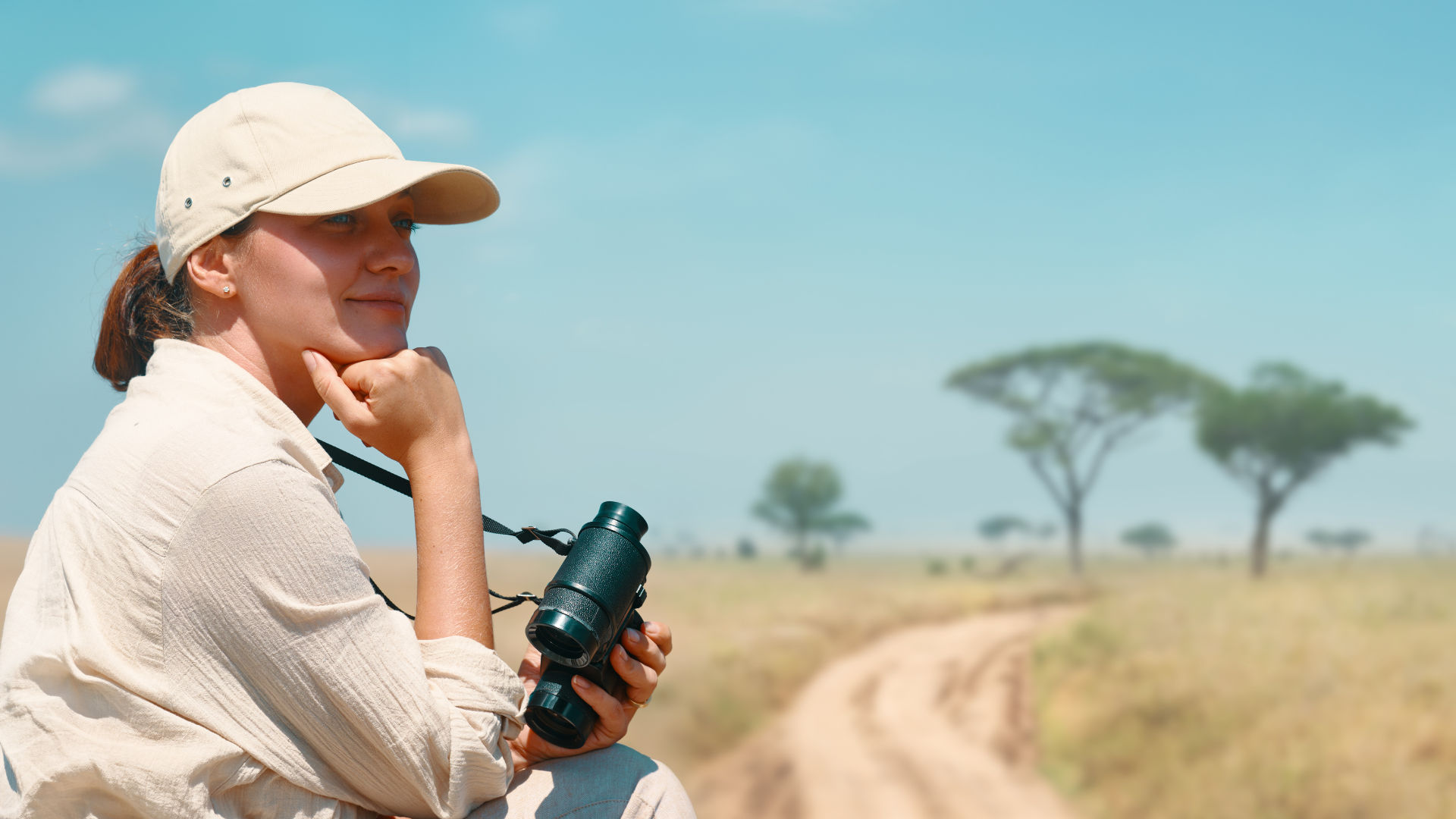 Woman with binoculars looking out at a safari landscape.