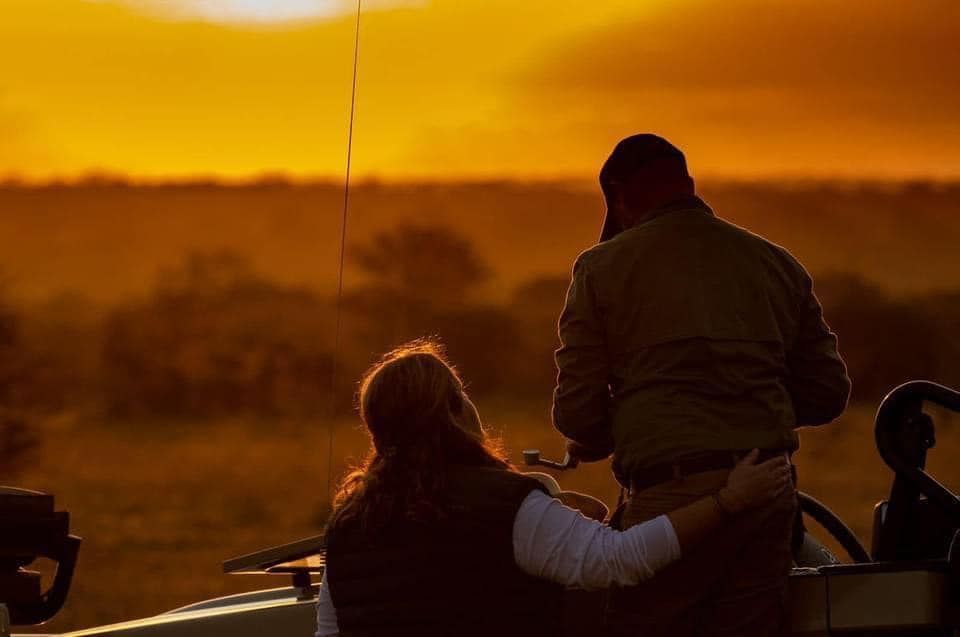 Couple on a safari vehicle, watching the sunset over the African savanna.