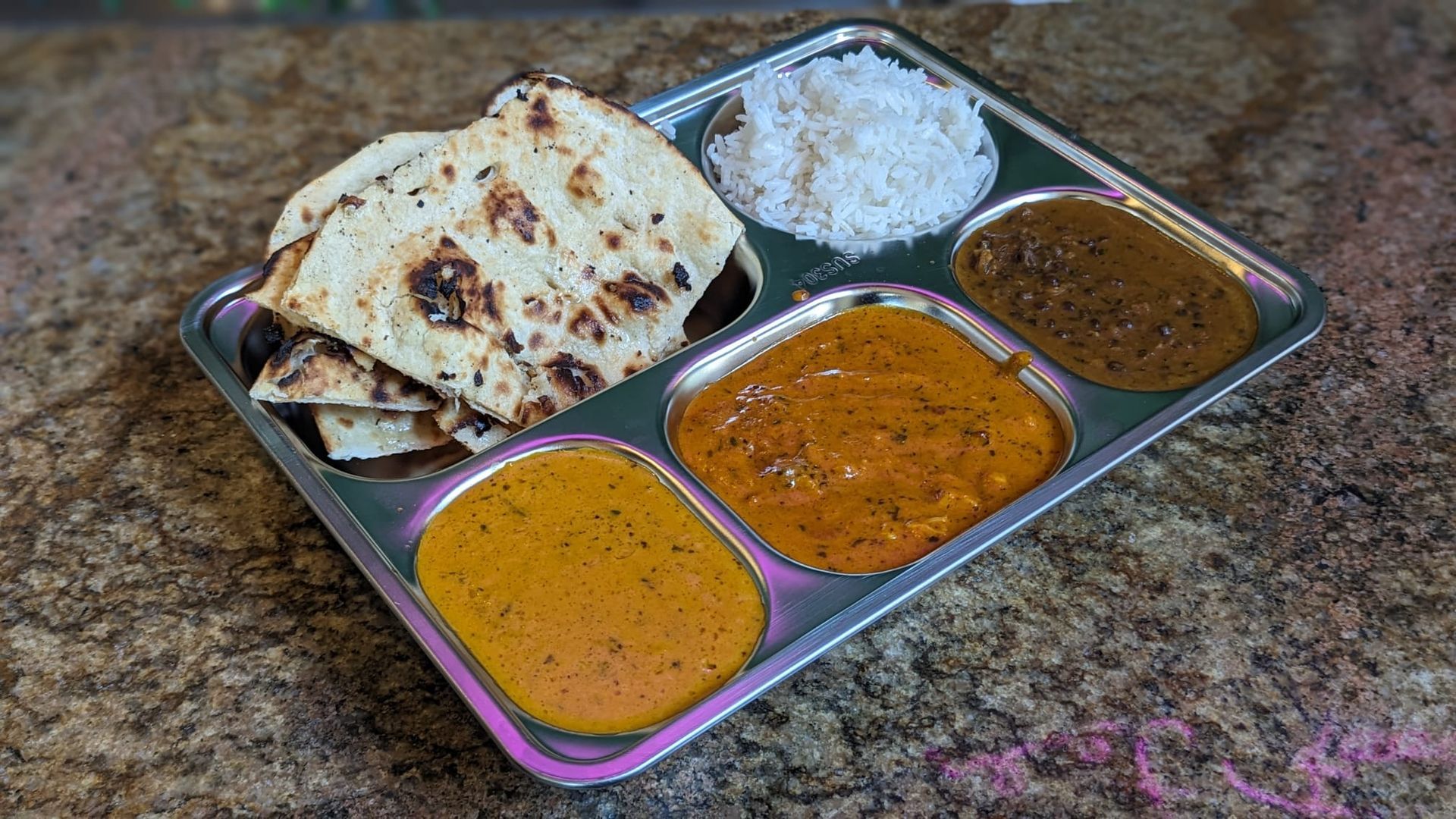 A tray of Indian food with bread , rice , and curry on a table.