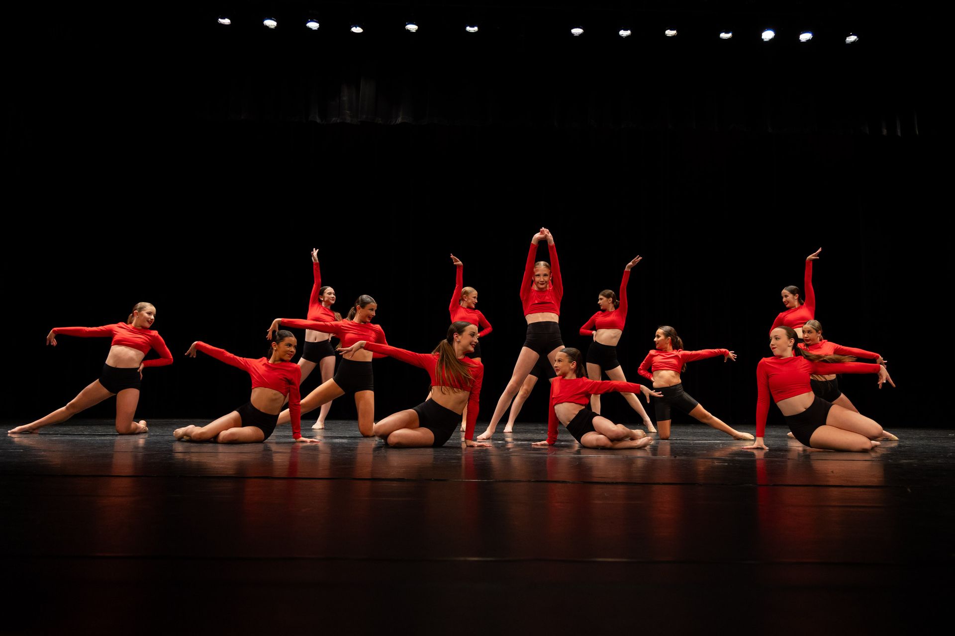 Group of dancers in red tops and black shorts performing on a stage.
