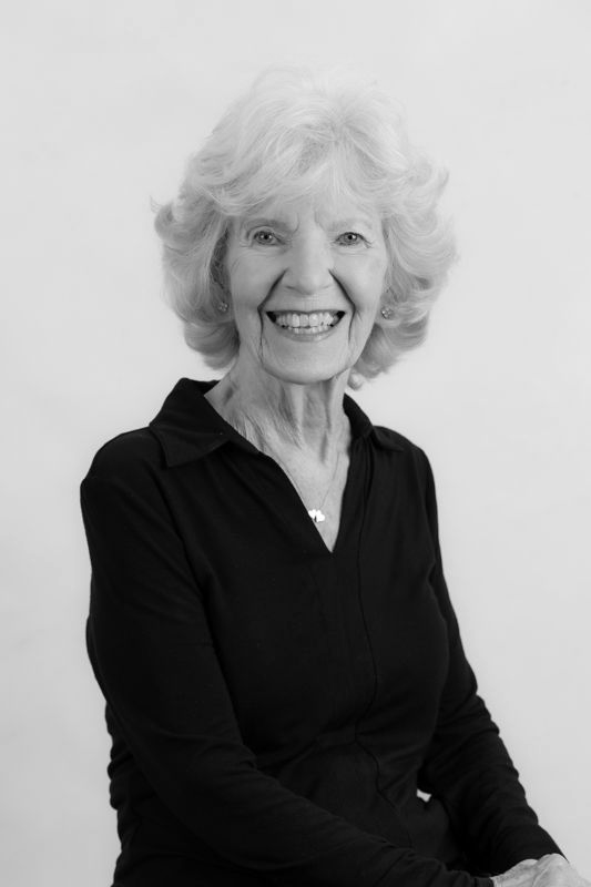 A woman with white hair is smiling in a black and white photo.