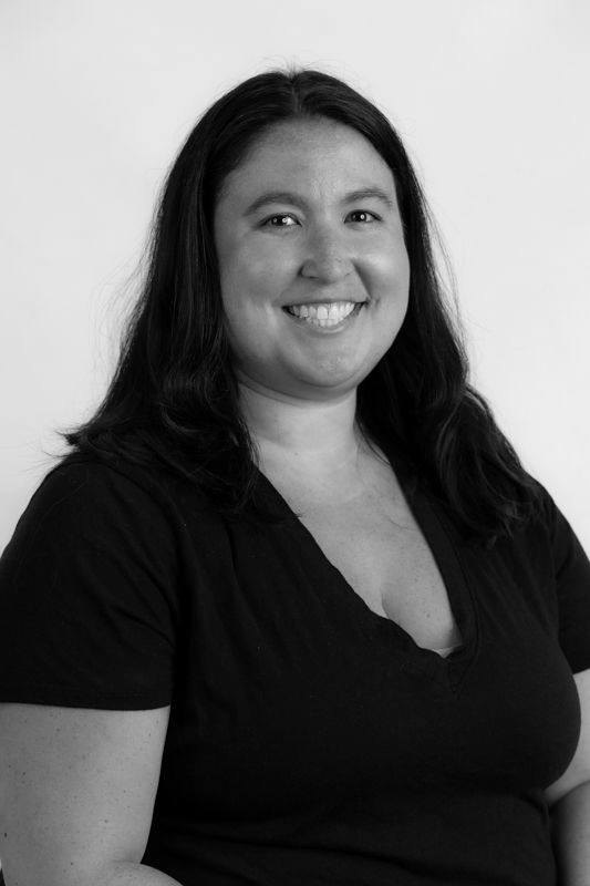 A woman in a black shirt is smiling in a black and white photo.