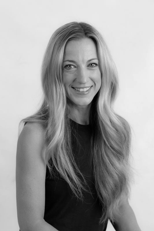 A woman with long blonde hair is wearing a black shirt and smiling in a black and white photo.