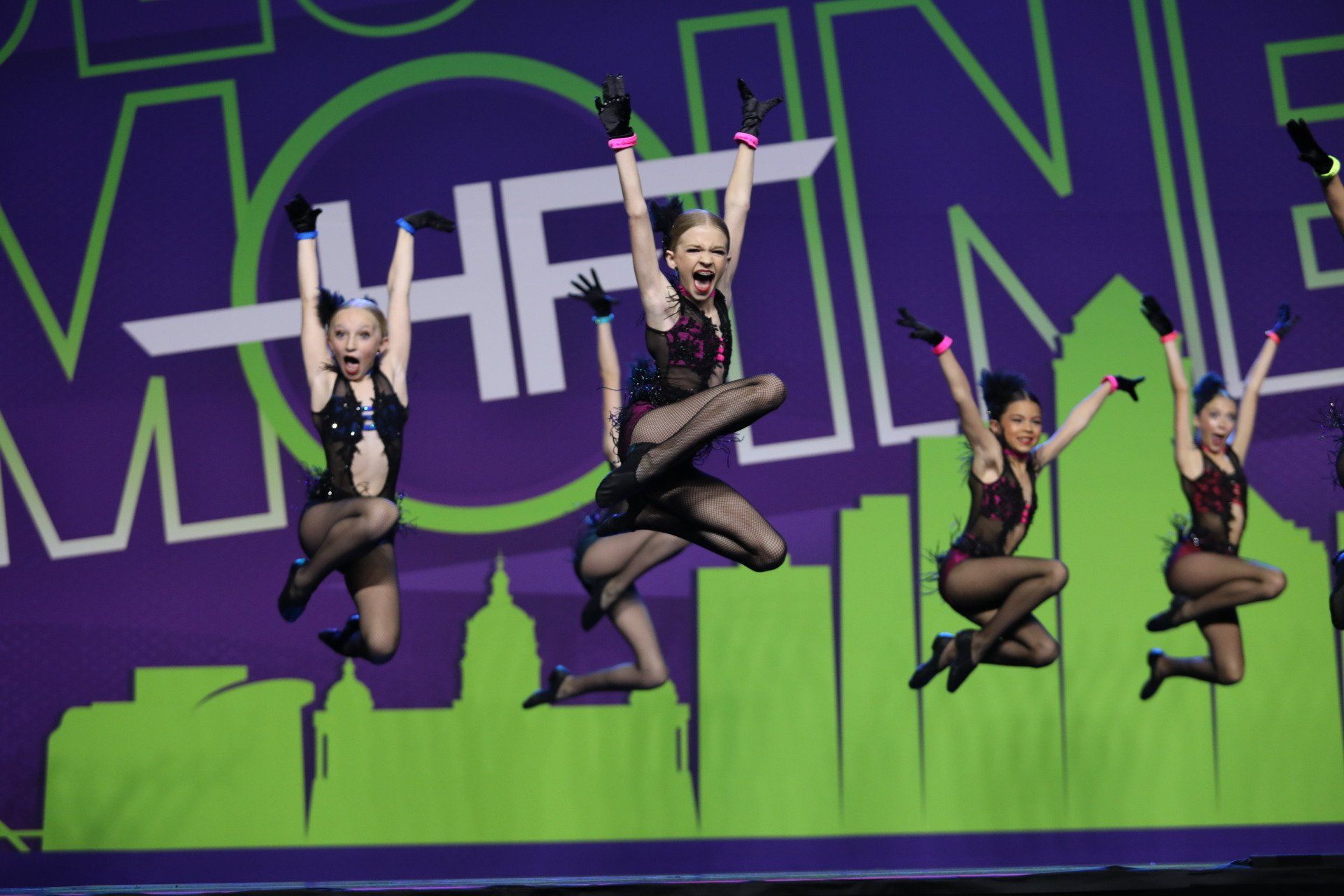 A group of young girls are jumping in the air on a stage.