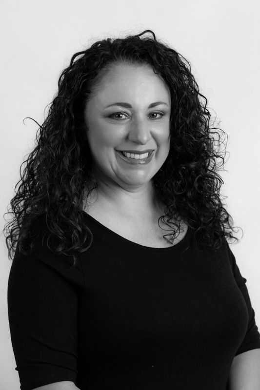A woman with curly hair is smiling in a black and white photo.