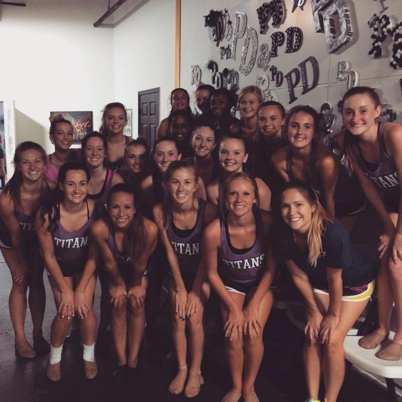 A group of women are posing for a picture and one of them is wearing a tank top that says titan