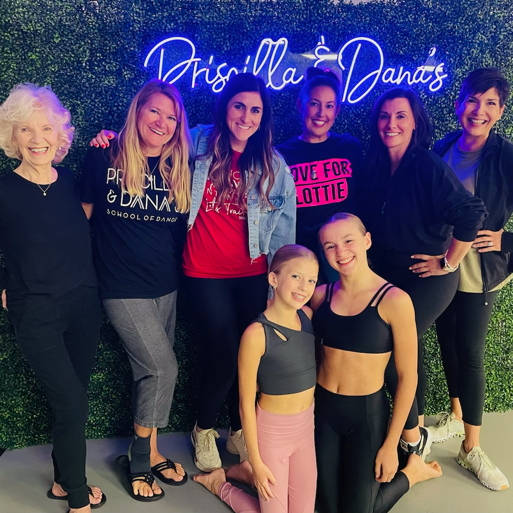 A group of women are posing for a picture in front of a neon sign that says priscilla dana 's