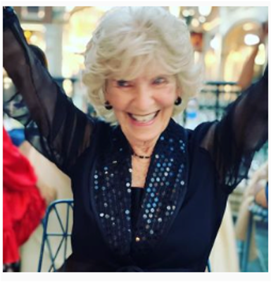 A woman in a black dress is smiling with her arms in the air