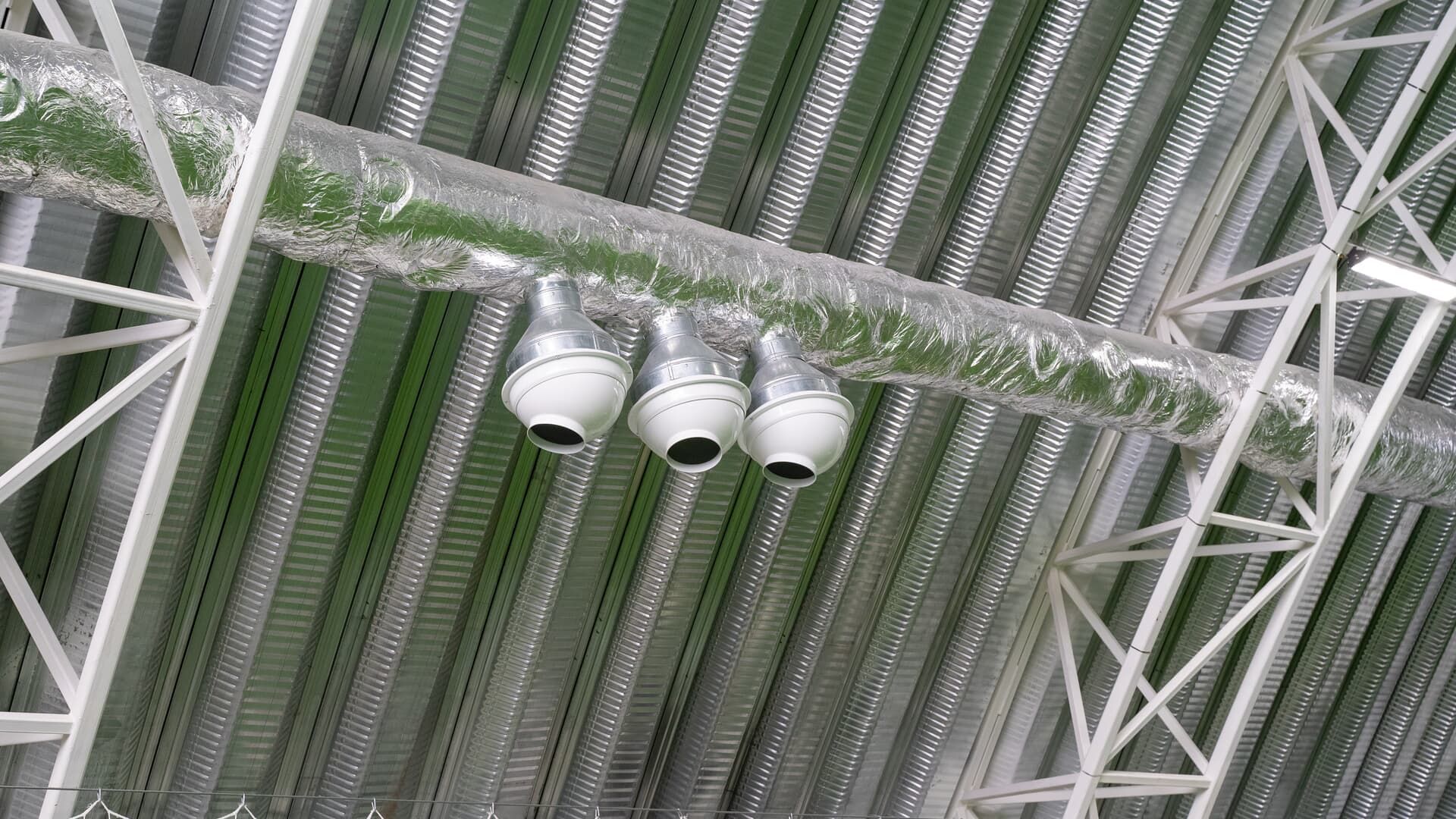 Three white dome security cameras mounted on a horizontal silver pipe attached to a metal corrugated ceiling.