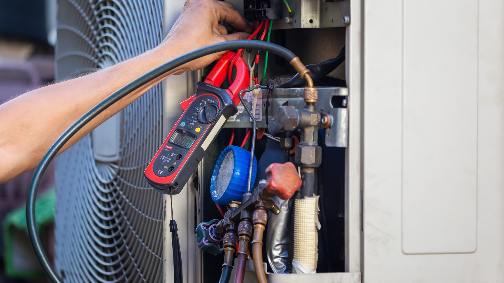 A technician using manifold gauges to check the refrigerant pressure on an outdoor air conditioning unit.