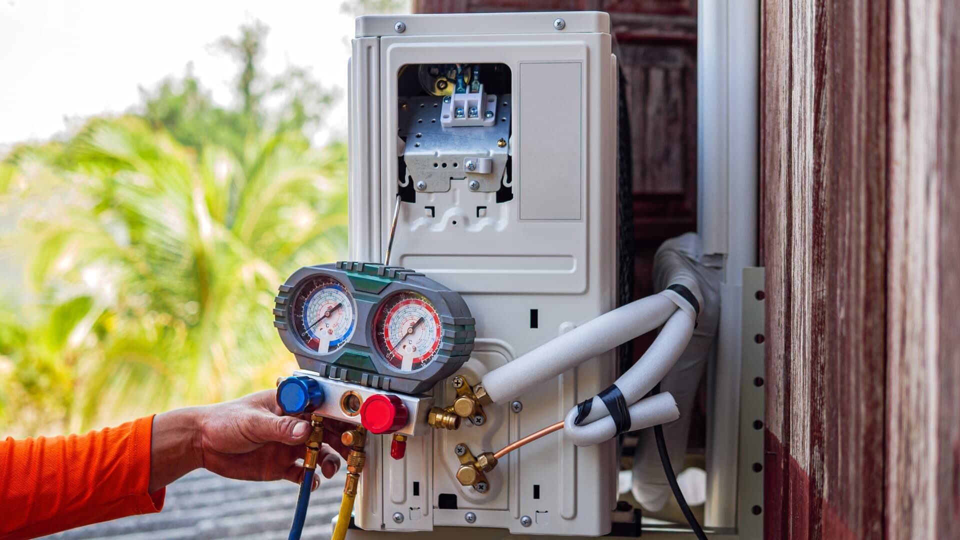 A technician uses a manifold gauge set to check refrigerant pressure on an outdoor air conditioning unit.