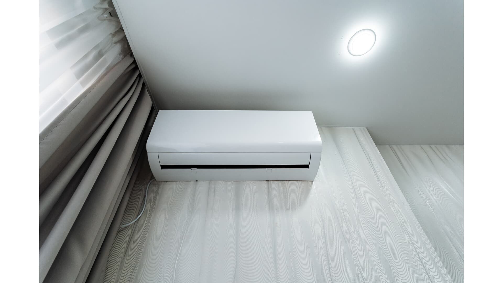 A white wall-mounted air conditioning unit installed above a window in a room.