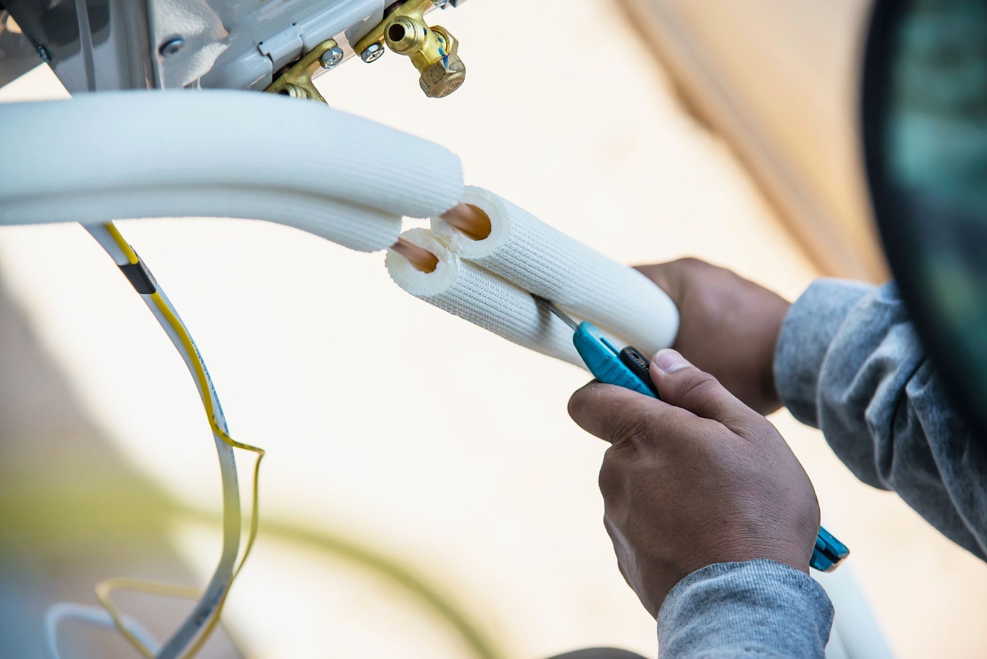 A person uses a utility knife to cut insulation on copper pipes for an HVAC system installation.