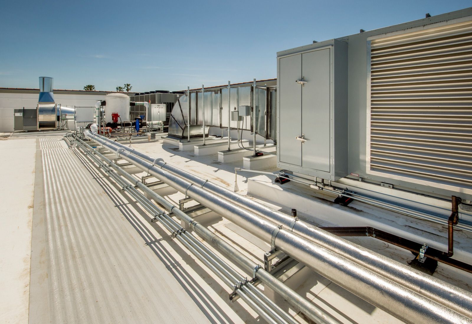 Industrial cooling units sit on a gravel ground next to an exterior building wall.