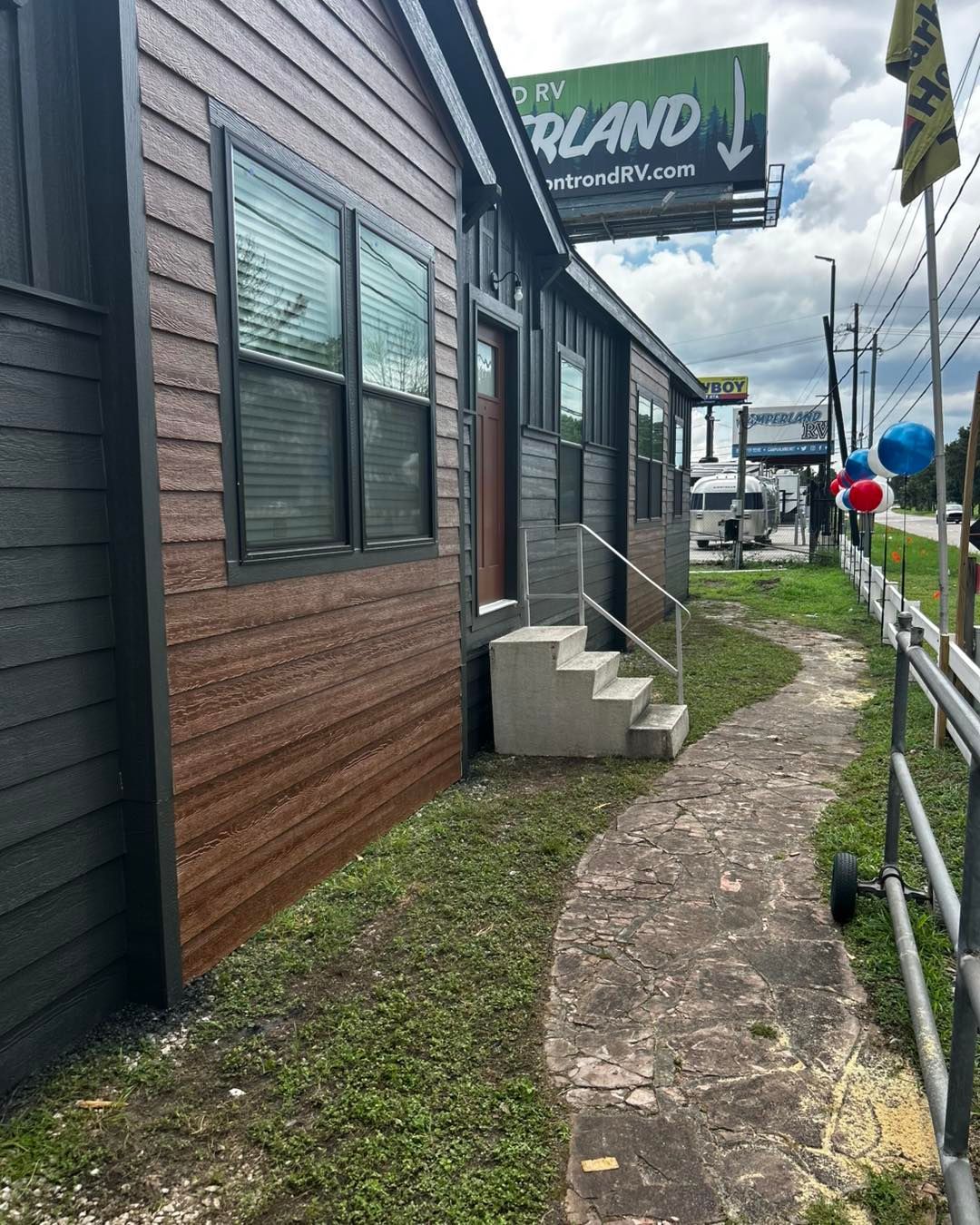 Small building with gray and brown siding, concrete path, and RV billboard.