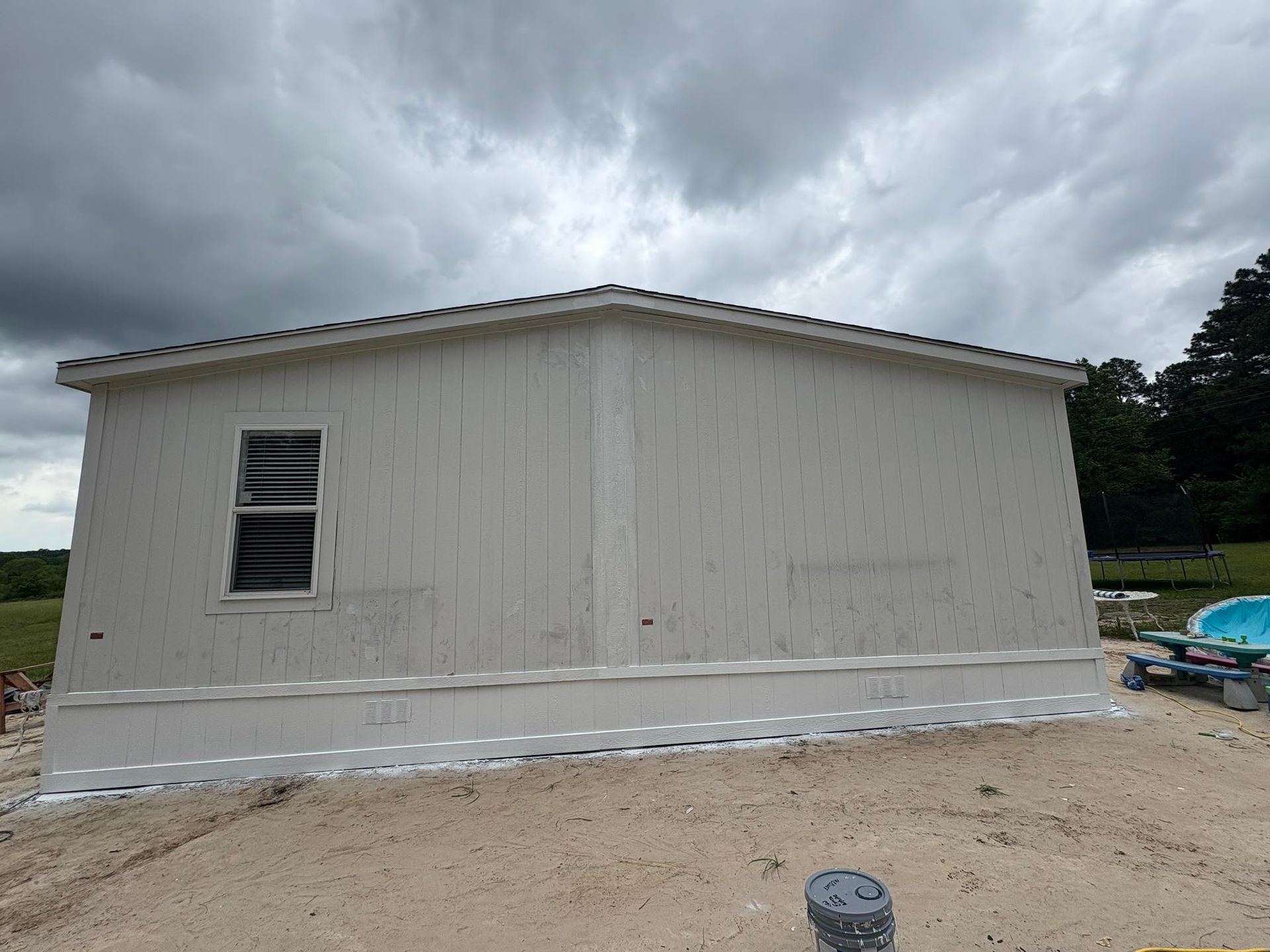 White-sided modular building under construction; window on the left side; cloudy sky in the background.