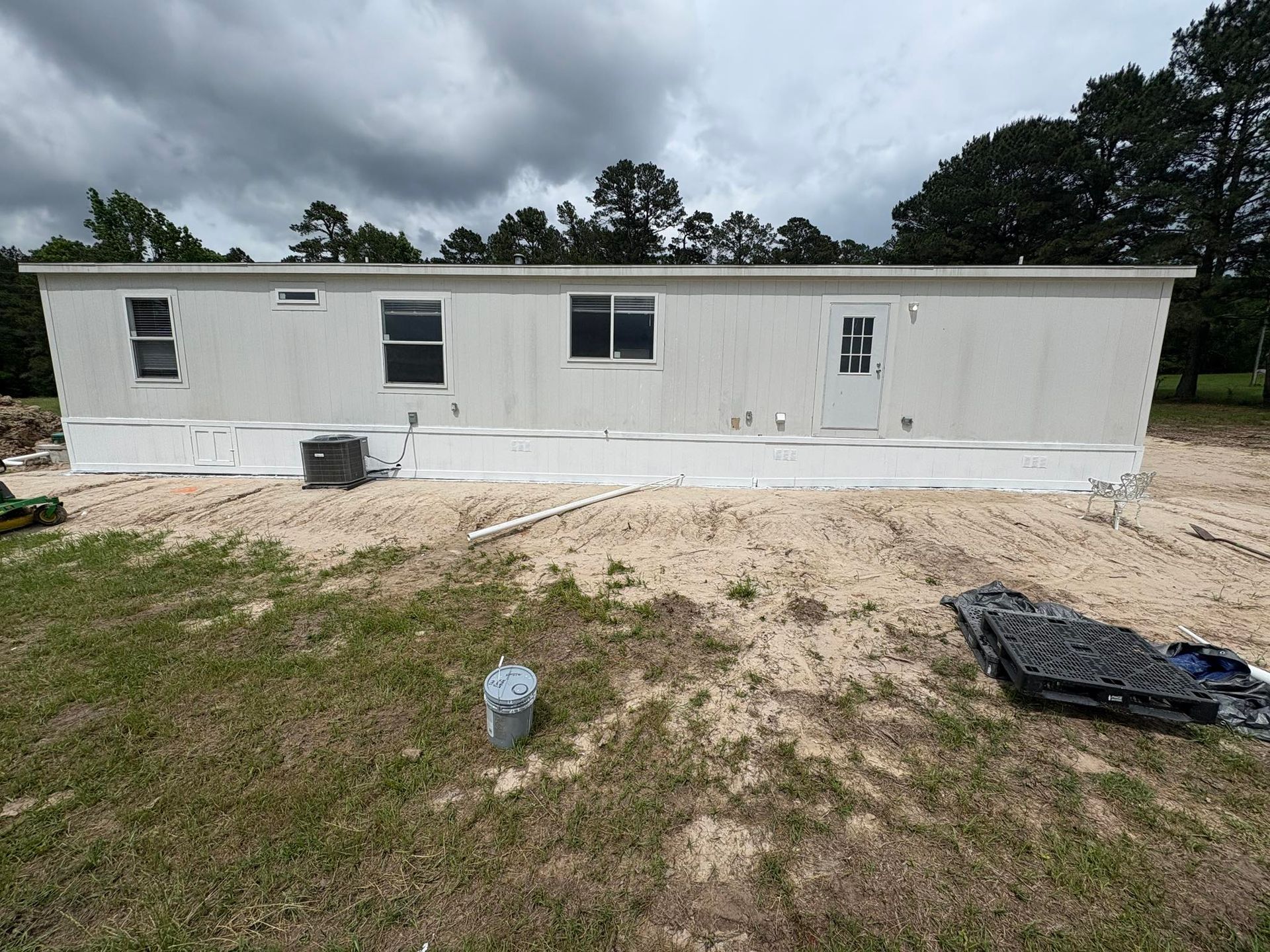 Mobile home on a sandy base, with windows, a door, and utility elements. Cloudy sky.