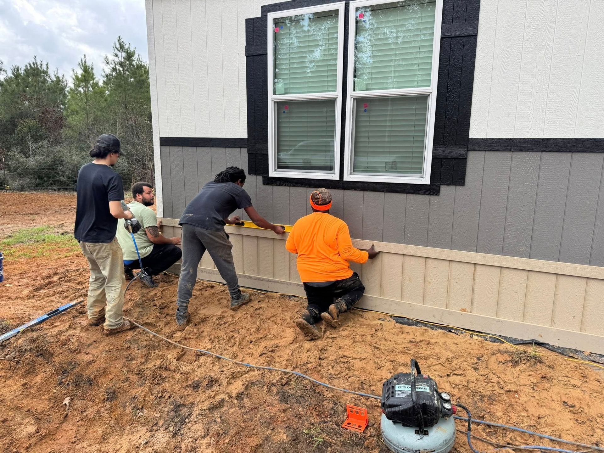 Construction workers installing beige siding on a house exterior, near a window.