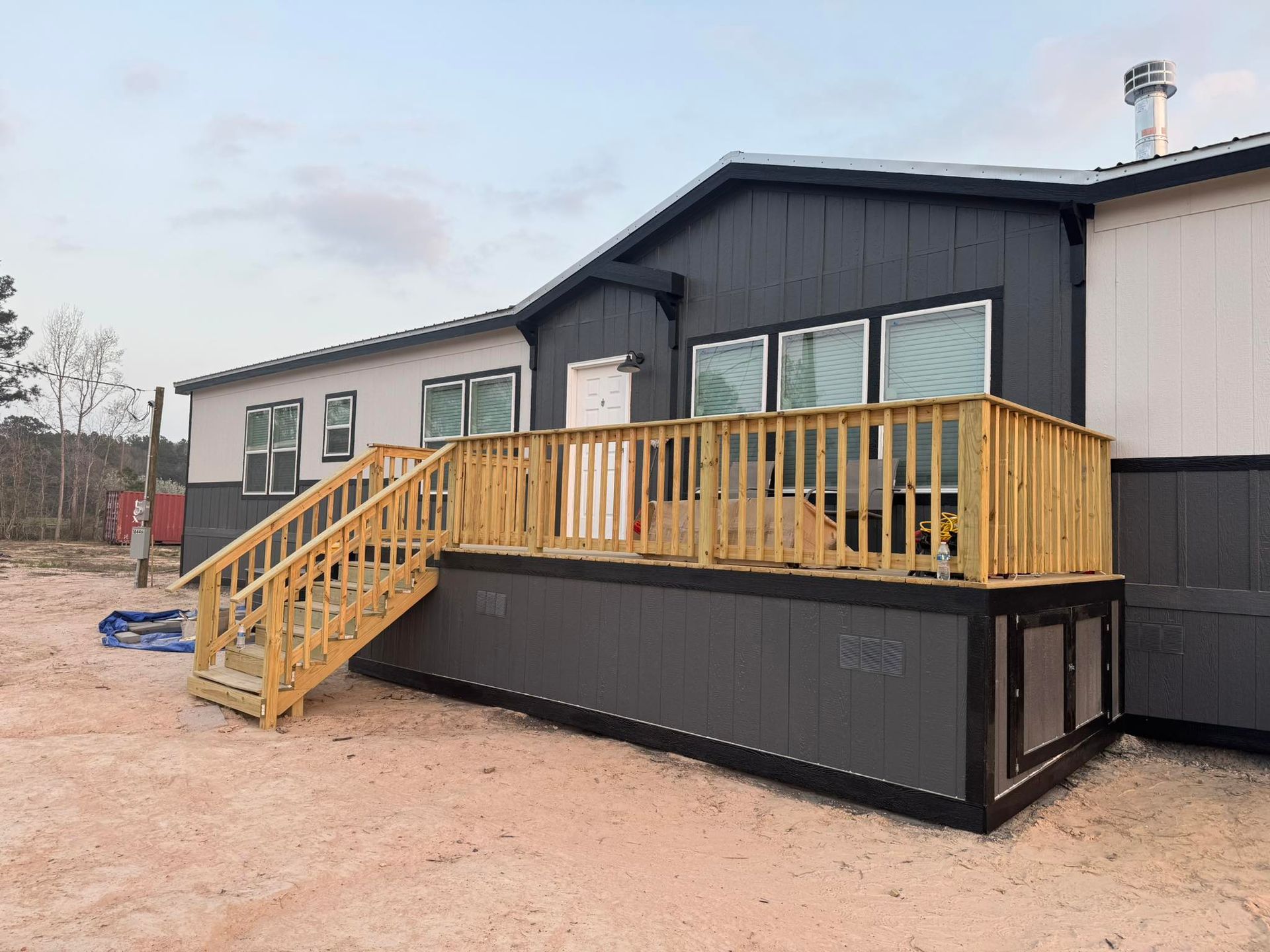 A house with a wooden deck and stairs. Gray siding and a light gray body.