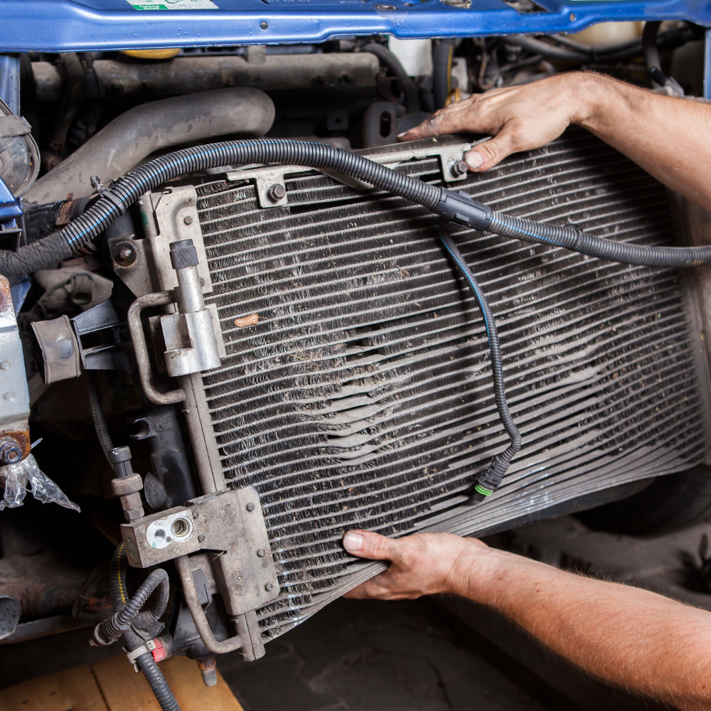 Hands removing a car radiator from an engine bay; close up.