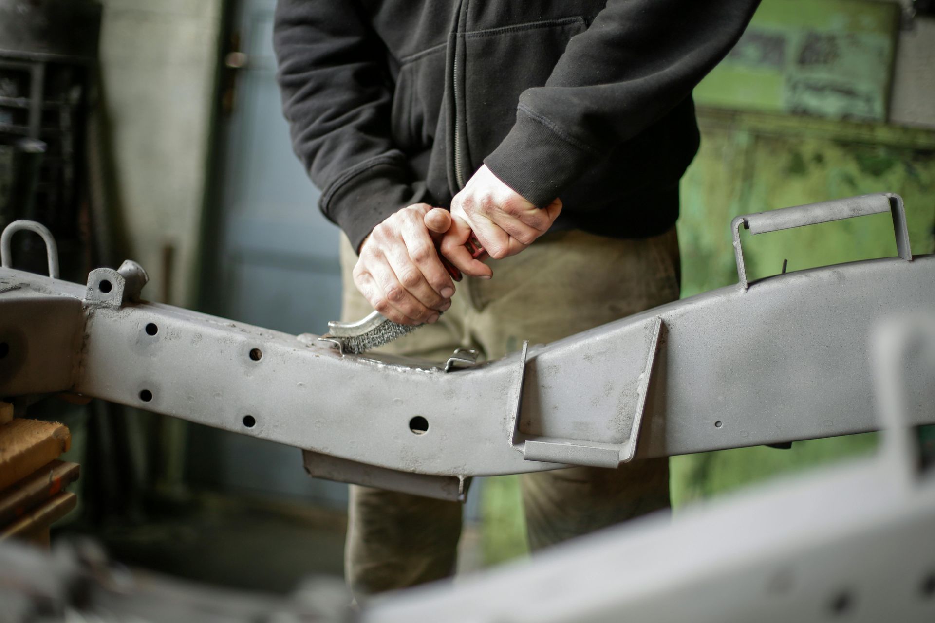 Person using a wrench on a gray metal vehicle frame in a workshop.