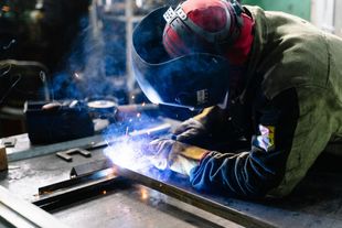 Welder in protective gear, welding metal with bright blue sparks.
