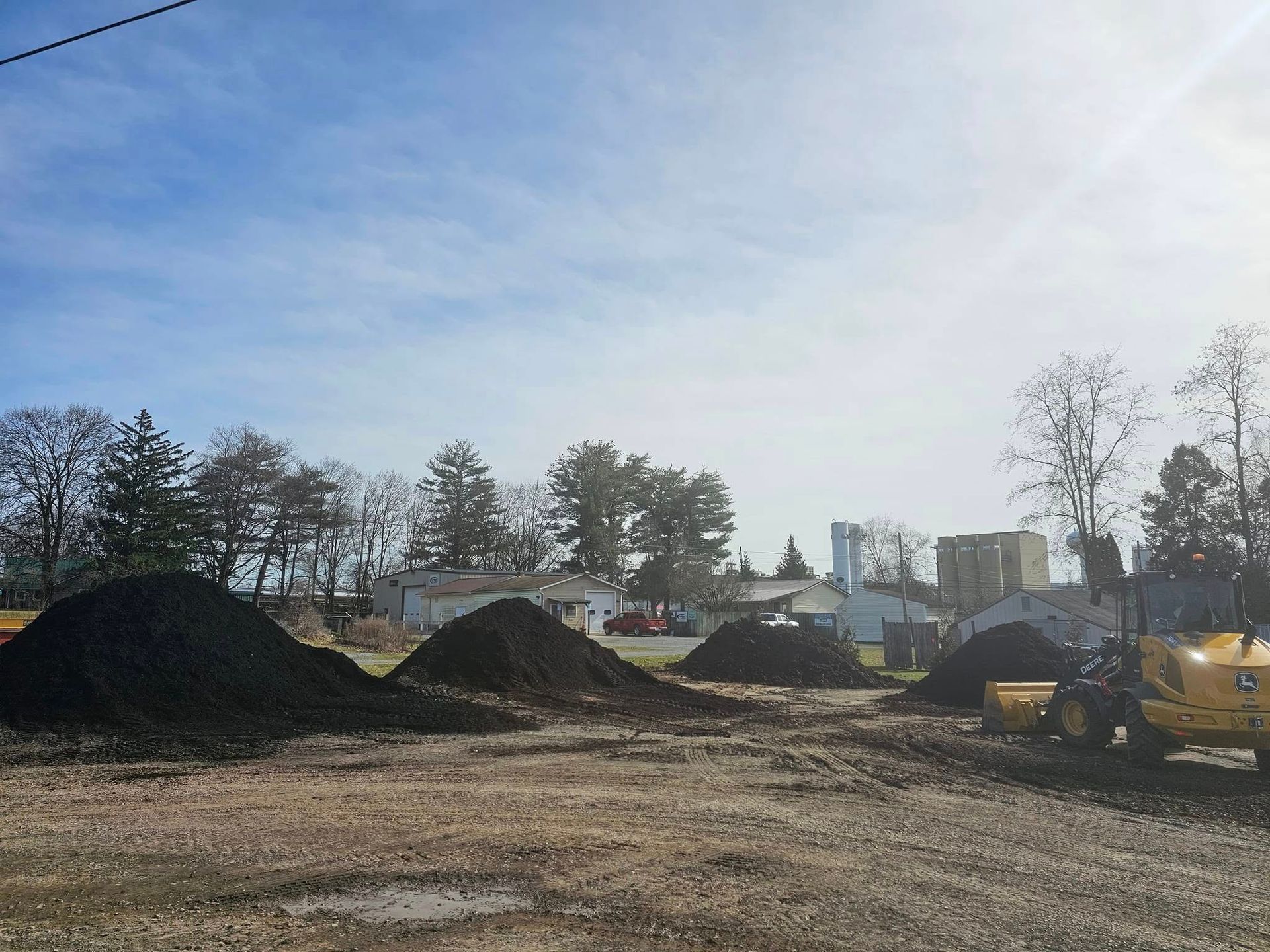 Construction site with dirt piles, excavators, and a partly cloudy sky