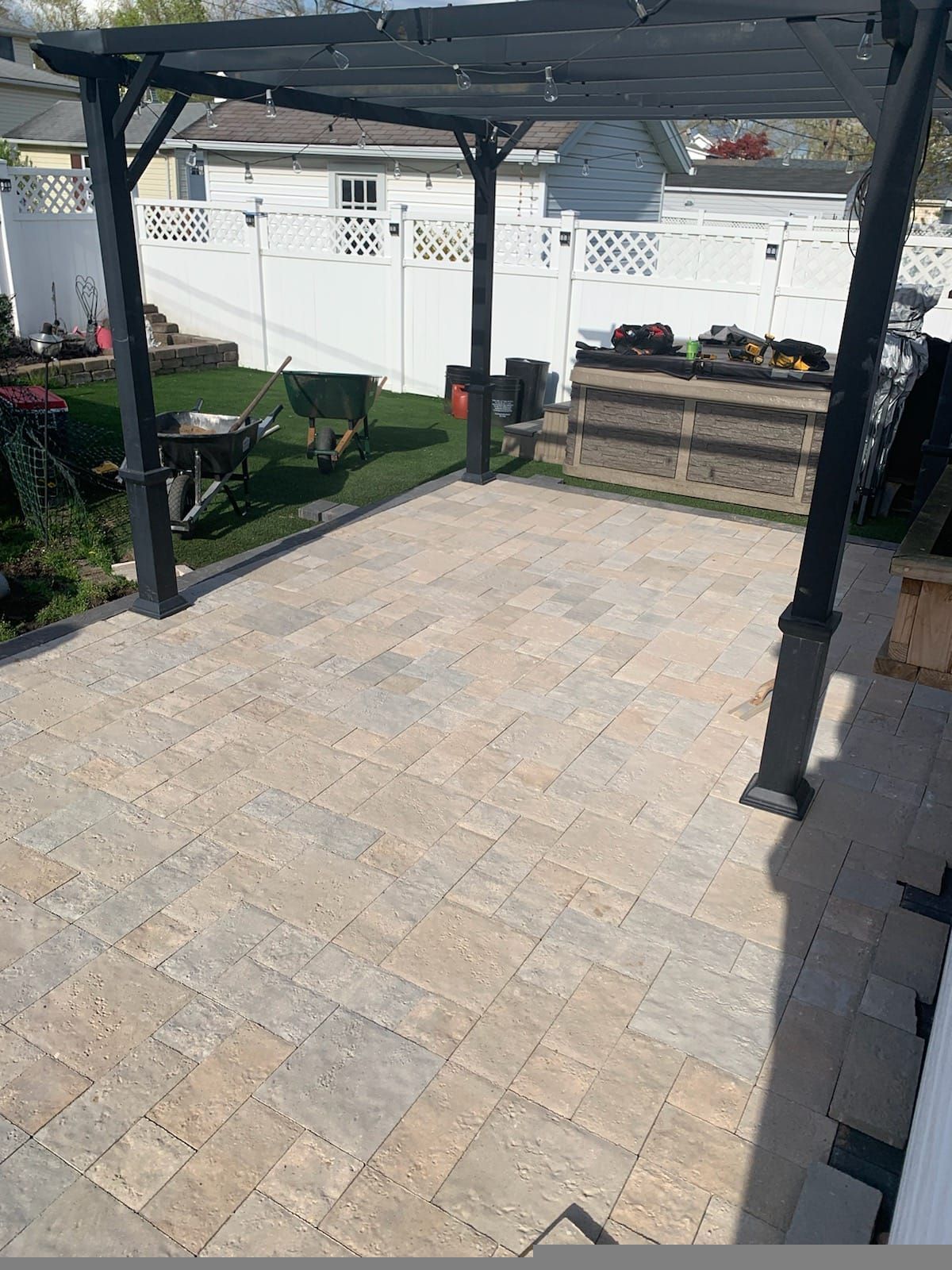 Covered patio with stone pavers, black posts, and raised garden beds beside a white fence.