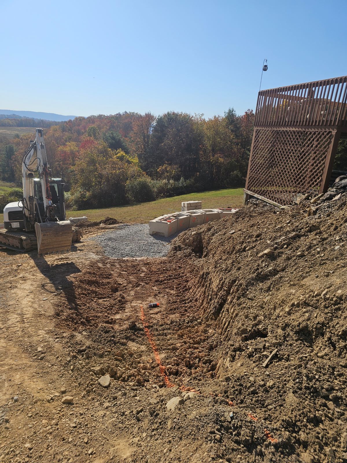 Excavator beside a dirt embankment at a construction site with autumn trees in the background
