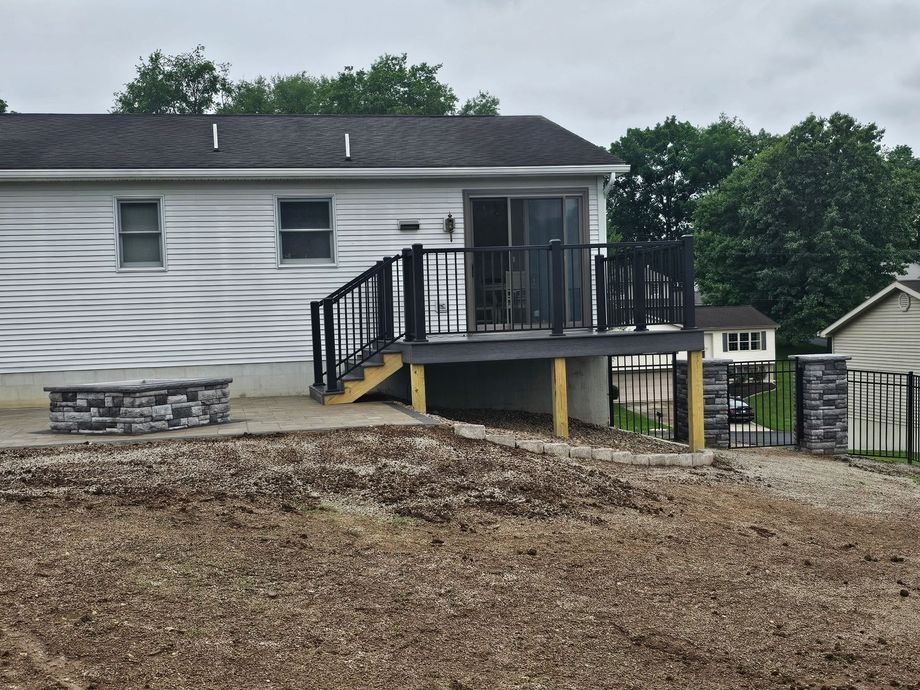 White house with black-railed deck on a gravel slope, viewed from the side.