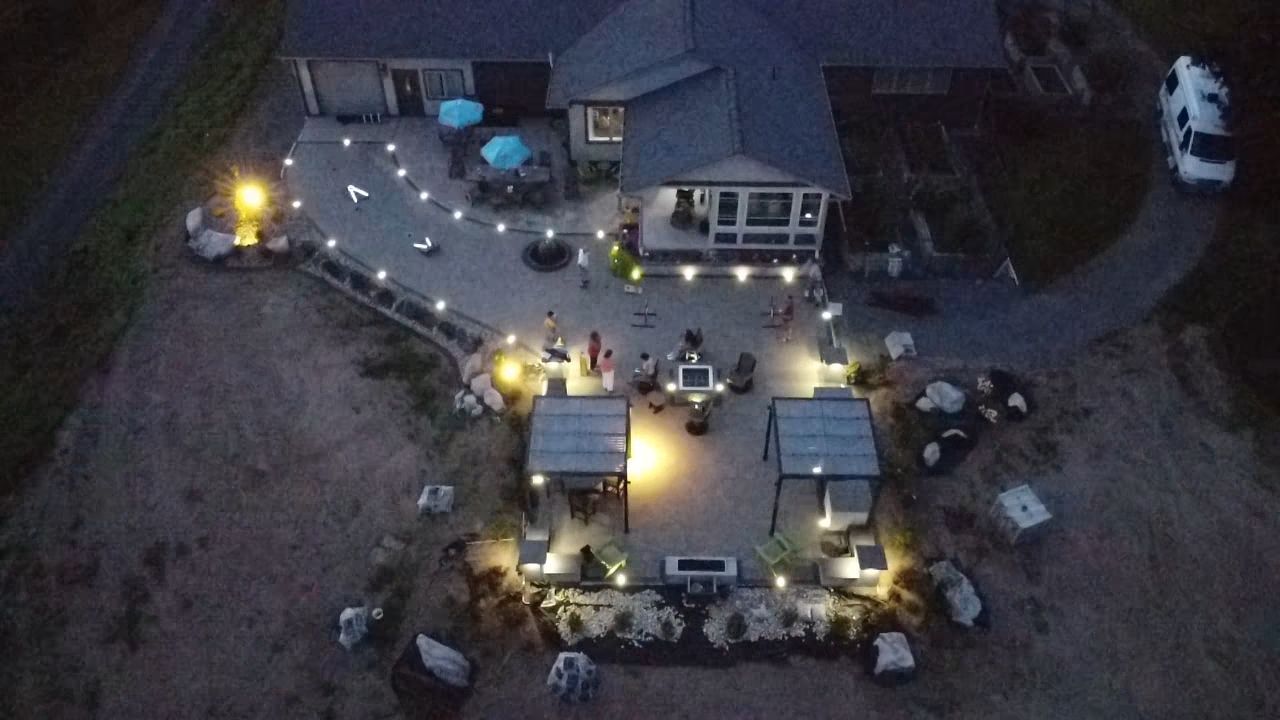 Aerial view of a lit outdoor gathering with tables and people at dusk near a house.