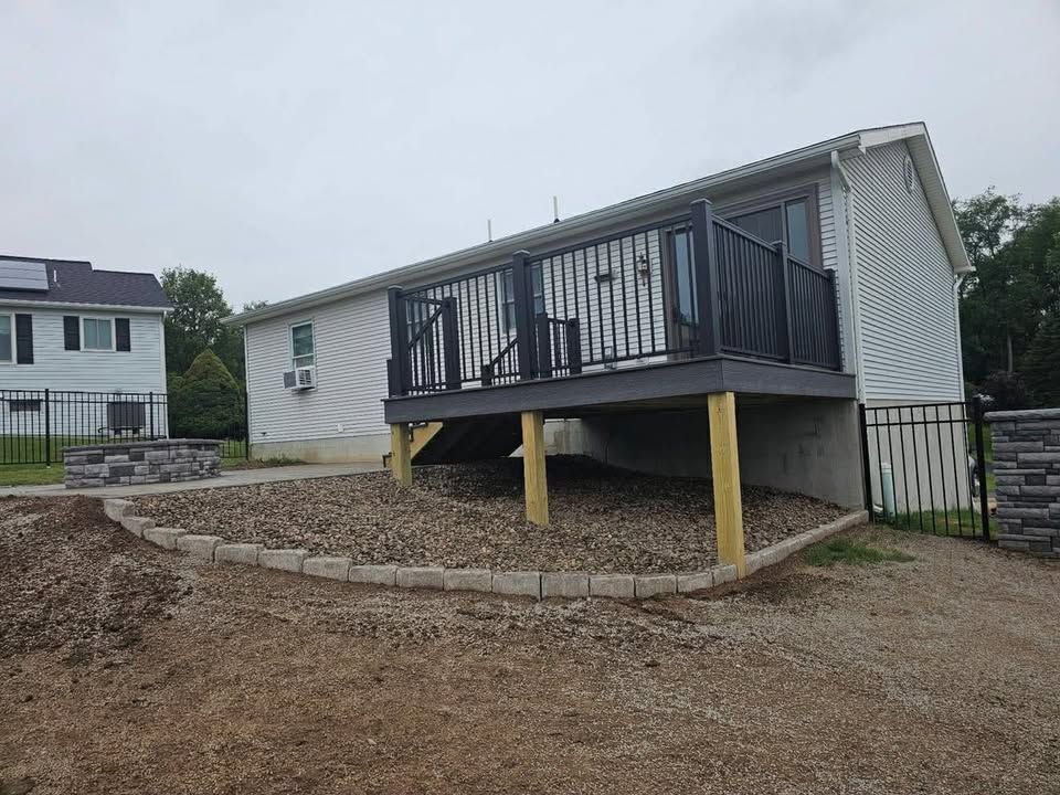 Raised porch deck with dark railings on yellow supports beside a gravel yard and house