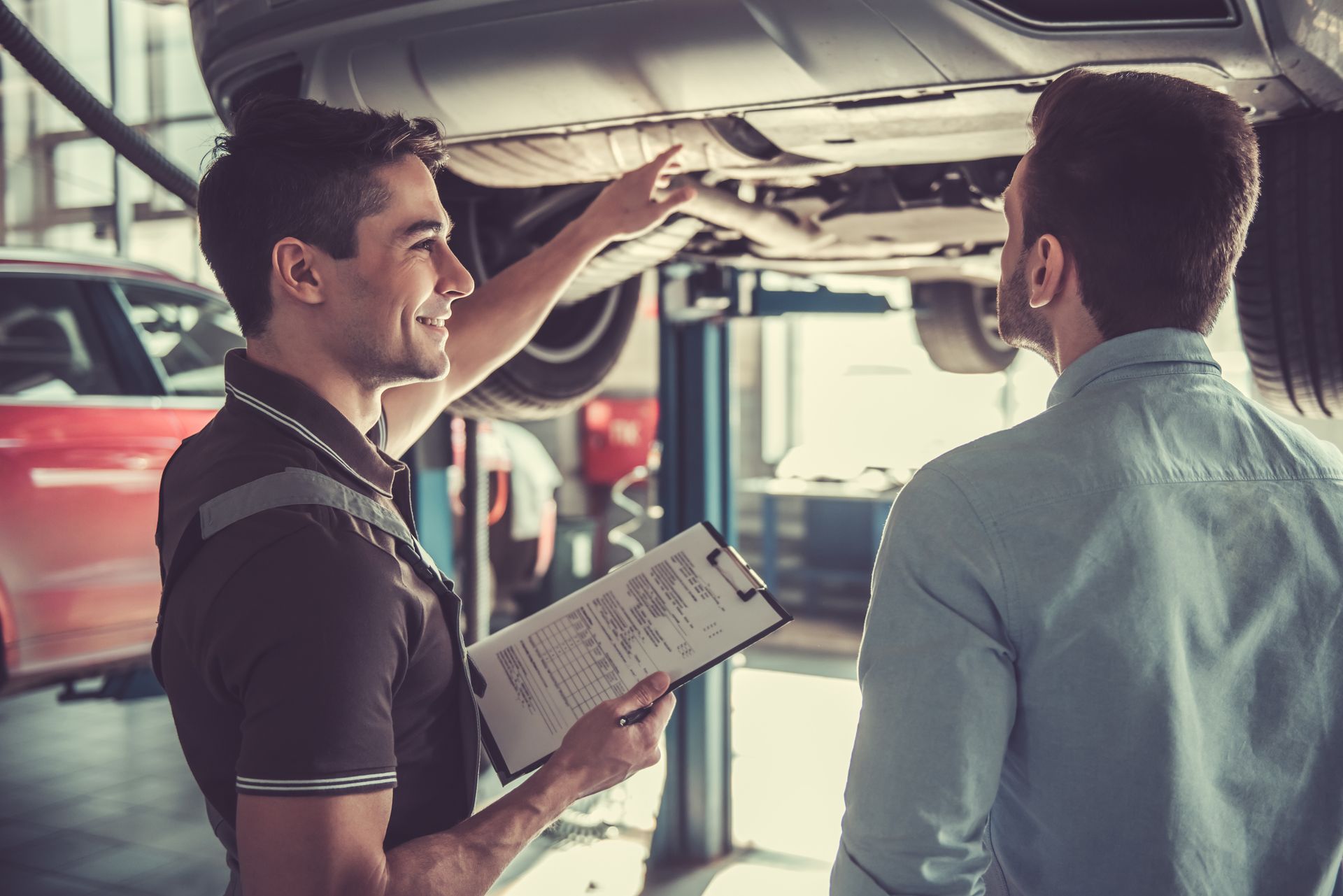 A brake shop technician explaining a vehicle undercarriage inspection to a customer.