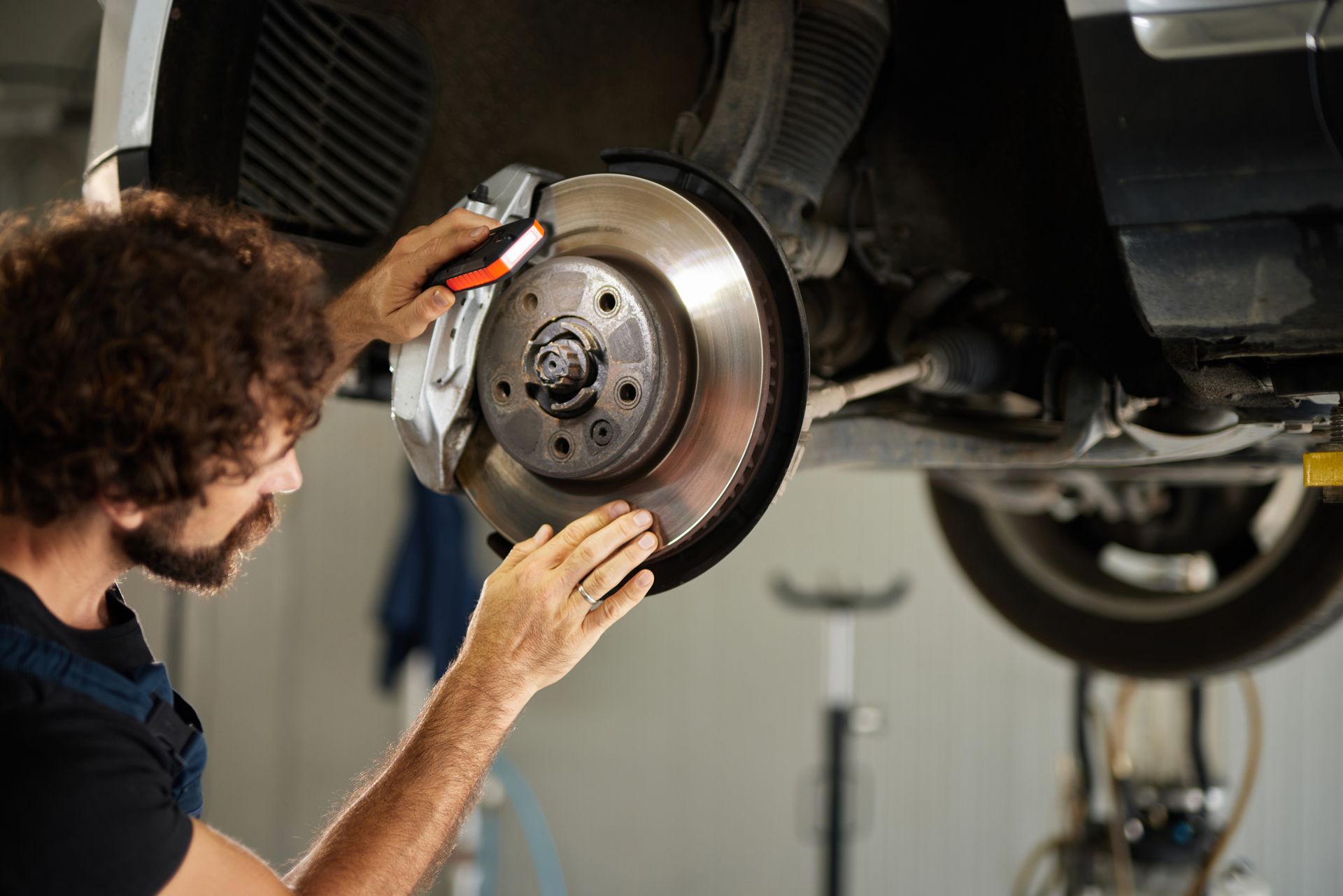 Mechanic inspecting and repairing car brake disc and caliper in auto brake shop.