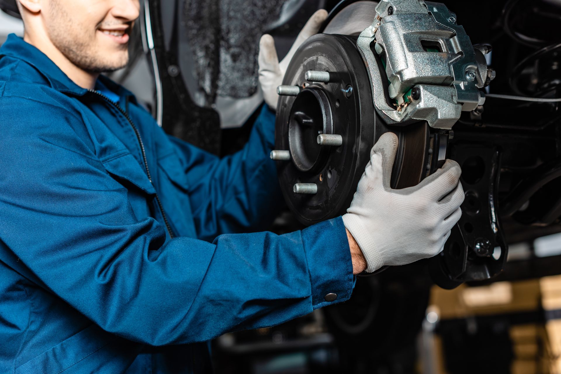 Worker installing a brake rotor and caliper on a car wheel hub in a repair shop. Worker installing a brake rotor and caliper on a car wheel hub in a repair shop.