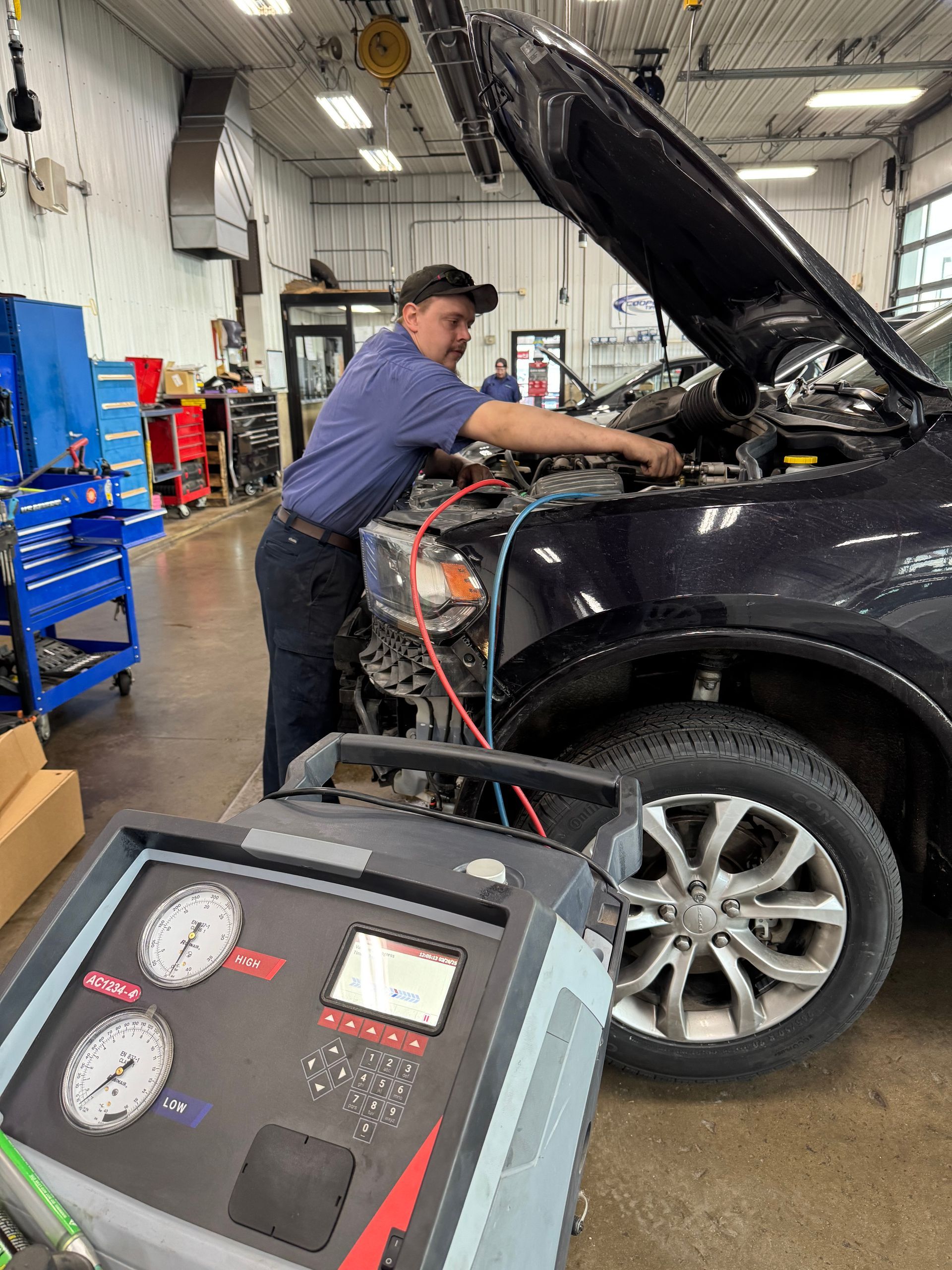 A man is working on a car in a garage with the hood up.