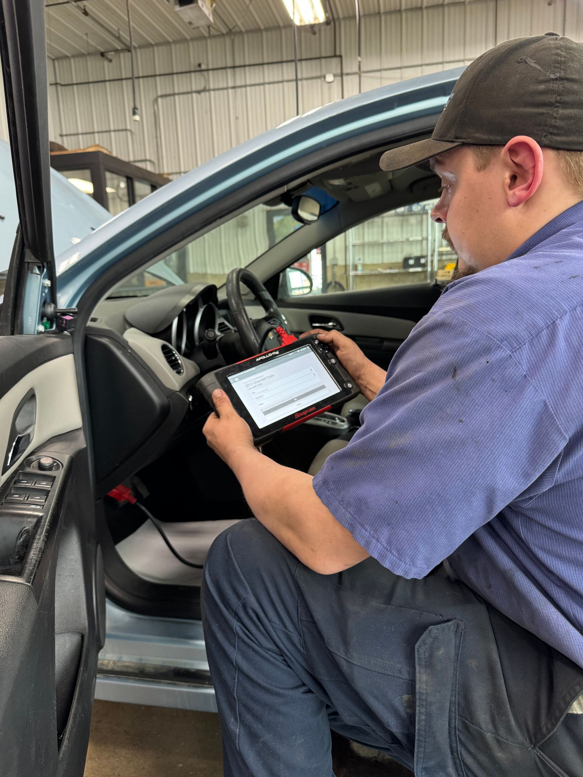 A mechanic is working on a car engine with a multimeter.
