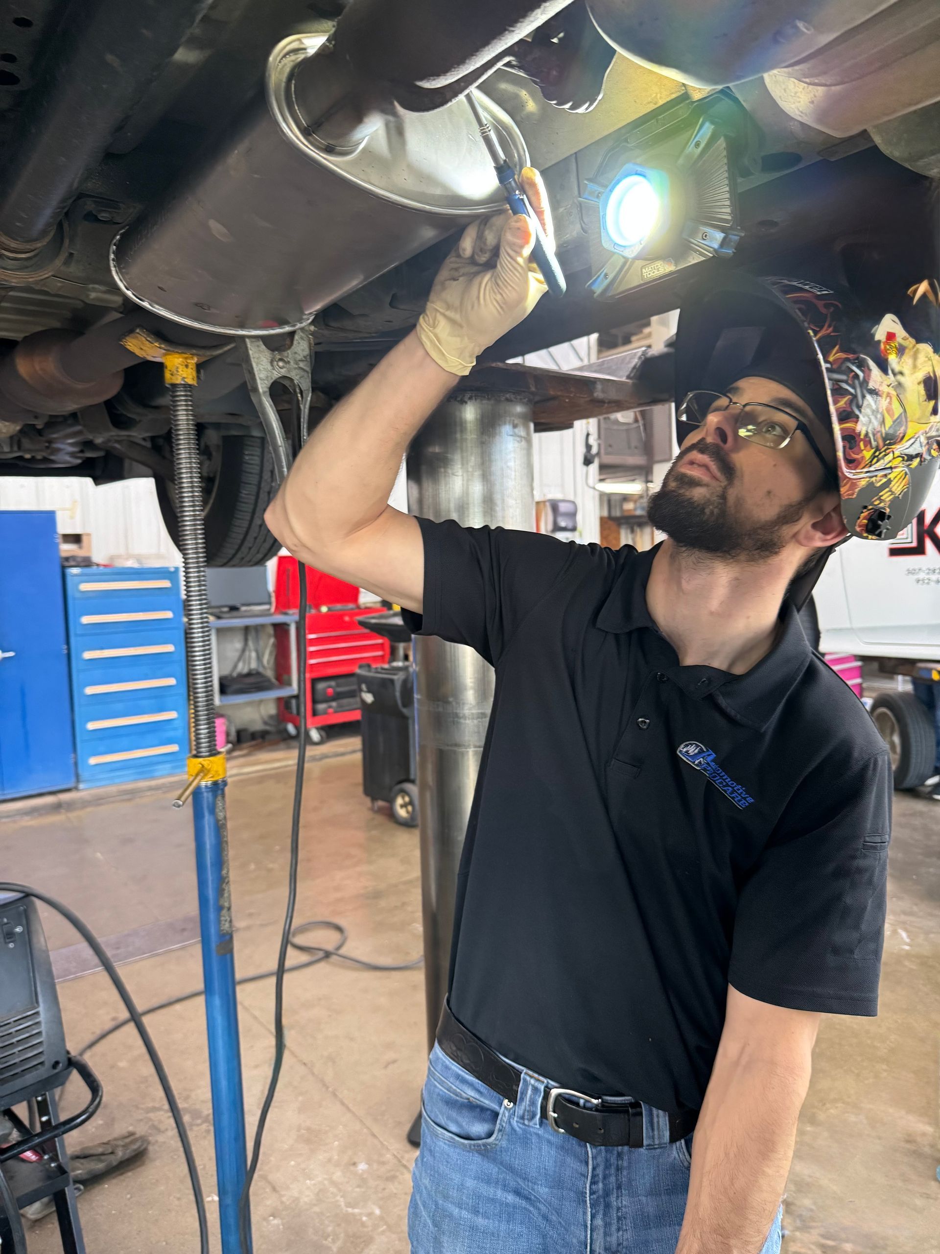 A man is welding a exhaust pipe under a car in a garage.