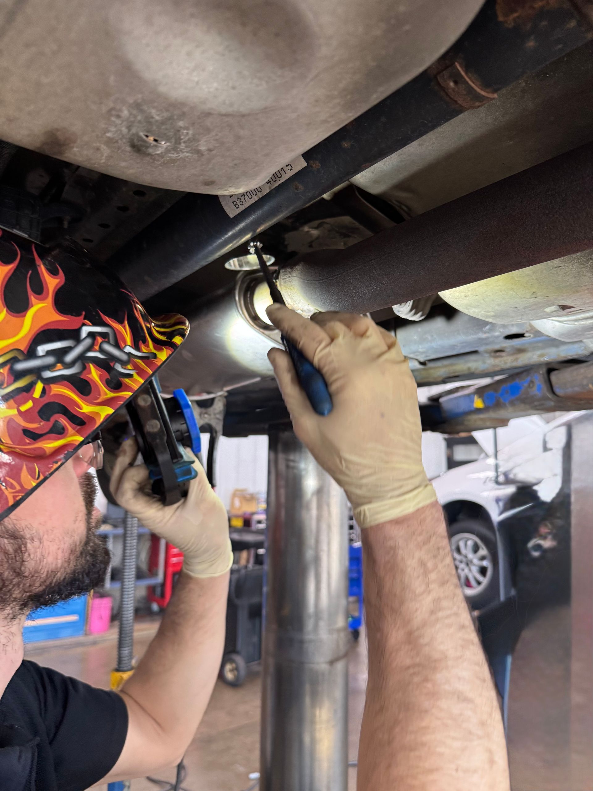 A man wearing a bandana with flames is working under a car