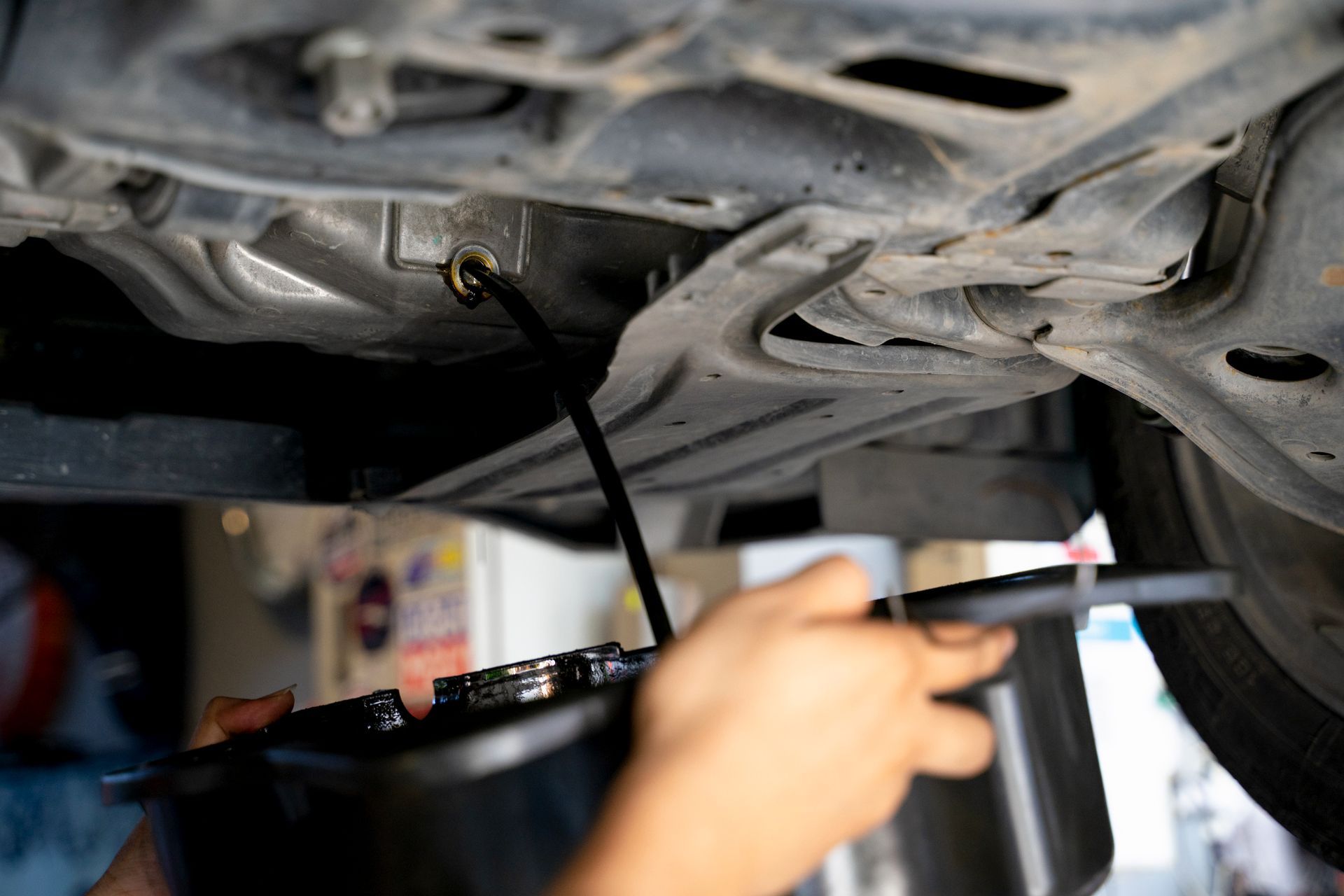 A person is pouring oil into a bucket under a car.