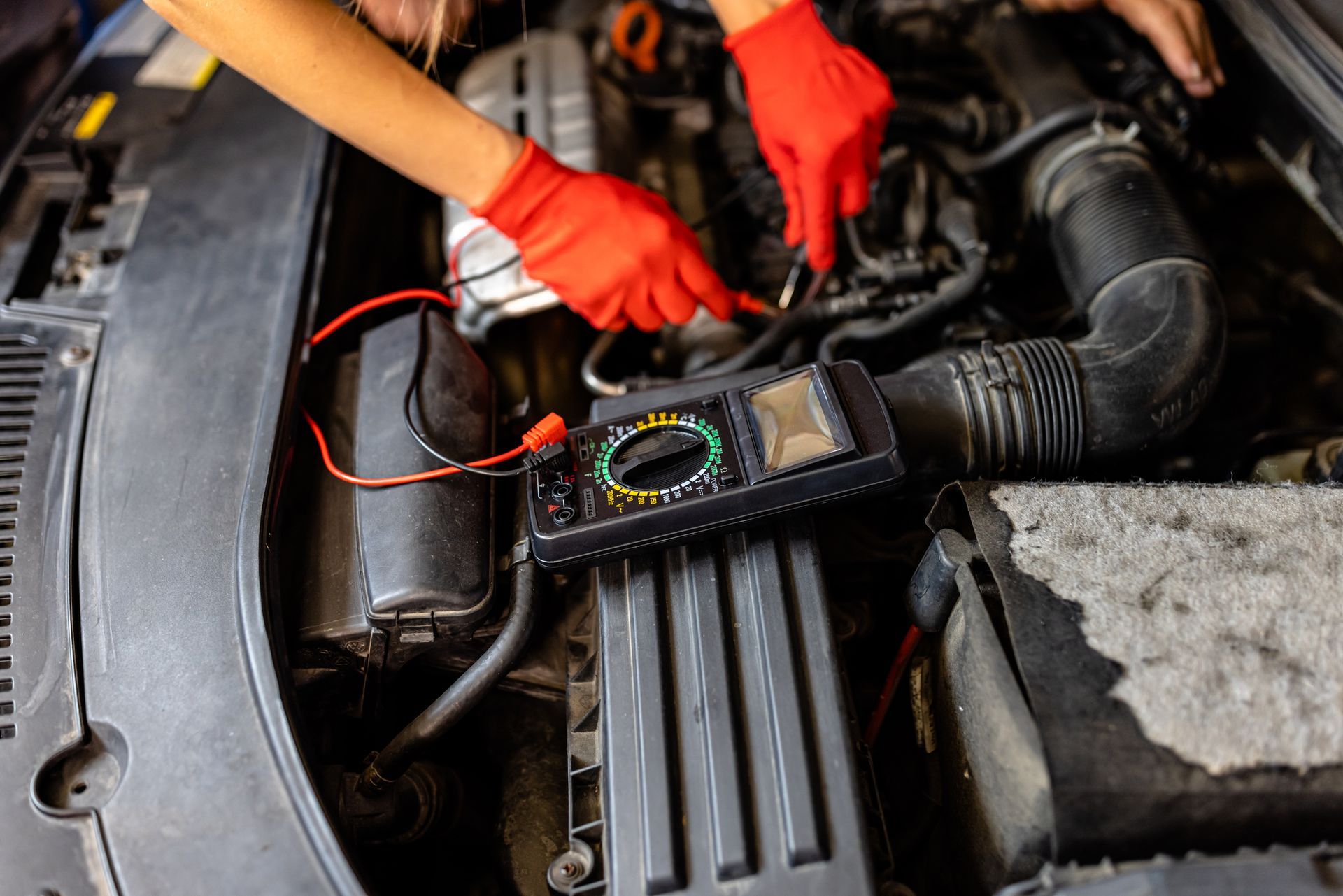 A person is working on a car engine with a multimeter.