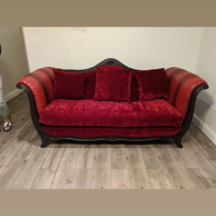Red velvet sofa with black trim and two pillows against a plain wall on a wood floor.