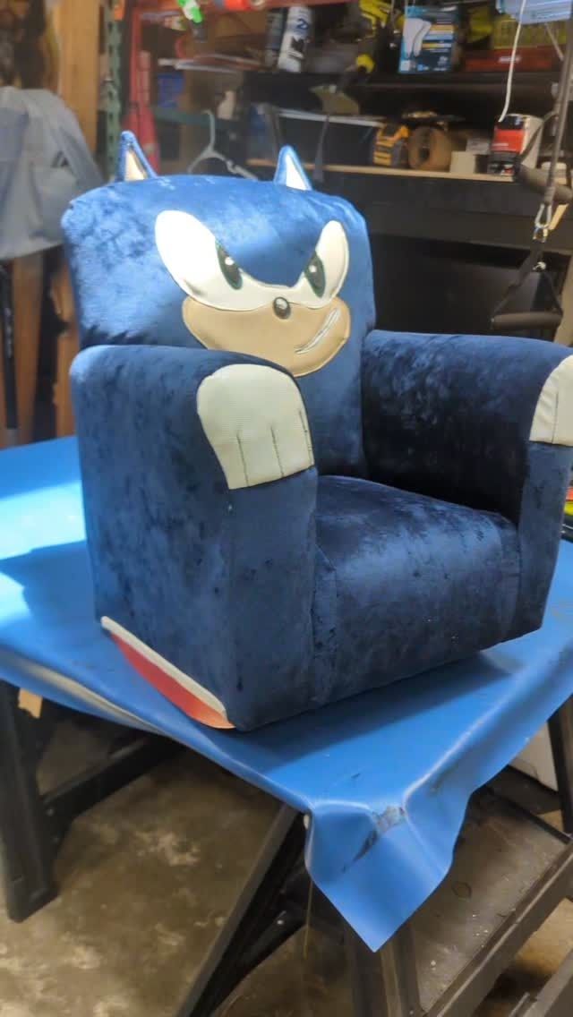 Blue Sonic-themed armchair with a plush face on the back, sitting on a table in a workshop.