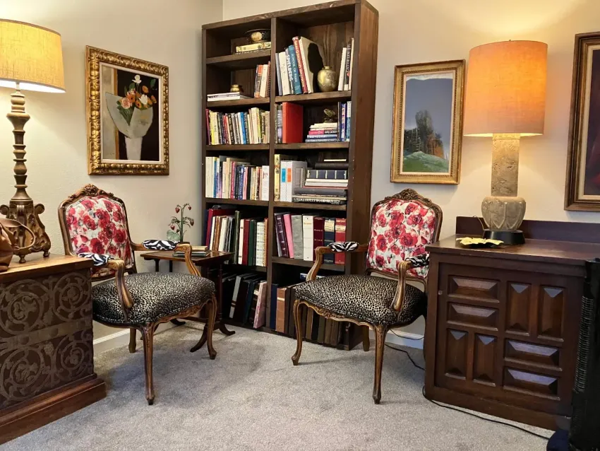 Cozy living room with floral chairs, bookshelves, framed art, and warm lamp lighting