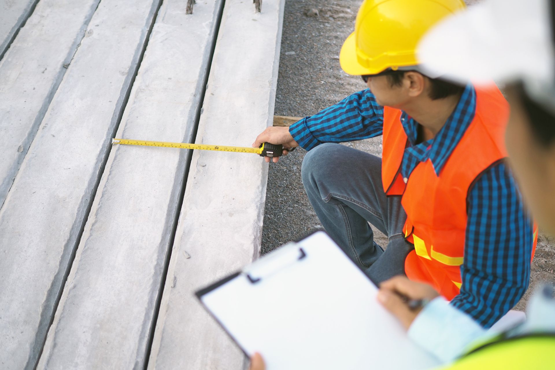 A construction worker is measuring a concrete slab with a tape measure.