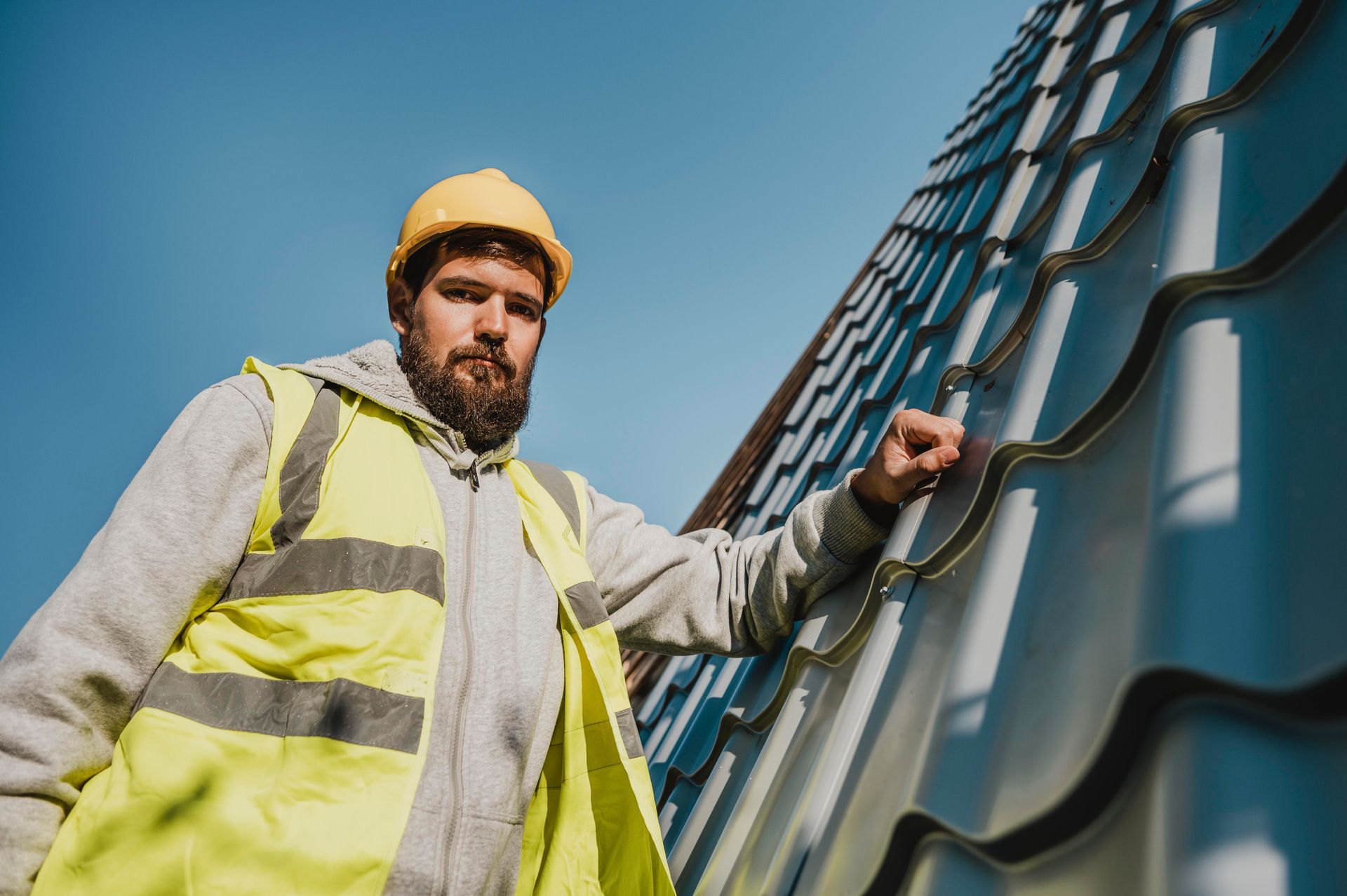 A man in a yellow vest and hard hat is standing on a roof.