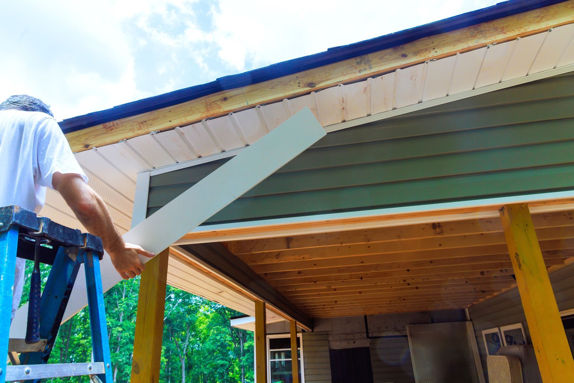 A man is standing on a ladder working on the roof of a house.